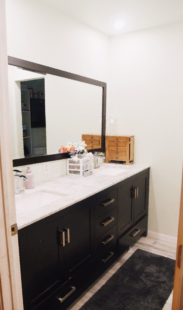 bathroom with double vanity, a sink, baseboards, and wood finished floors
