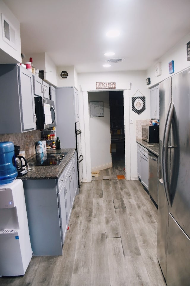 kitchen featuring dark stone counters, backsplash, stainless steel appliances, and light wood-type flooring