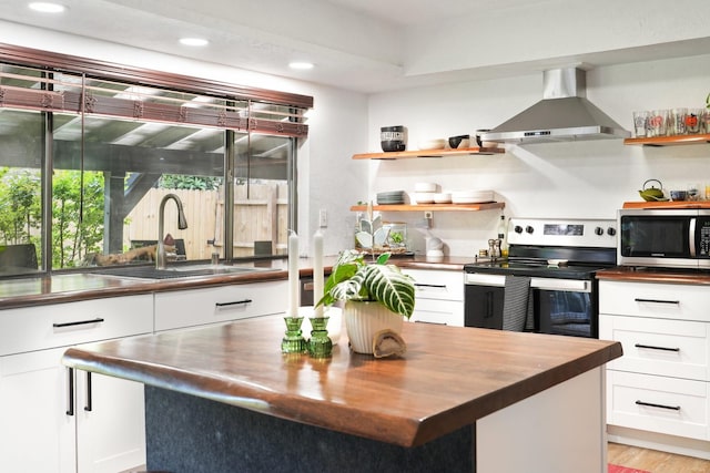 kitchen with wall chimney range hood, open shelves, a sink, butcher block counters, and stainless steel appliances