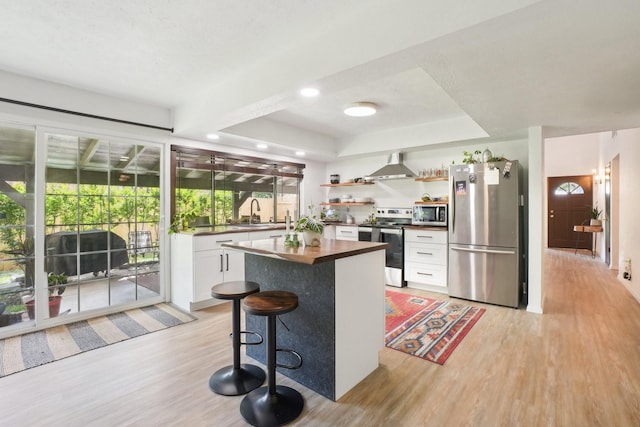kitchen featuring wooden counters, appliances with stainless steel finishes, light wood finished floors, wall chimney exhaust hood, and white cabinetry