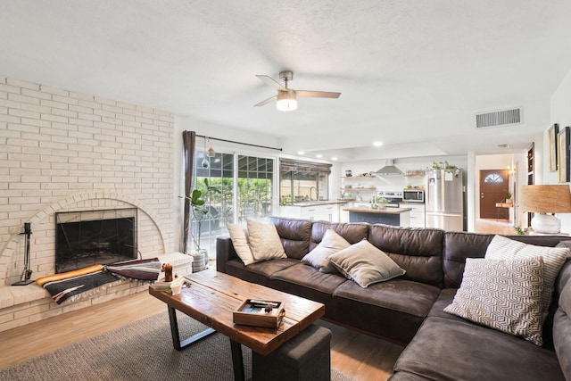 living room featuring ceiling fan, wood finished floors, visible vents, and a fireplace