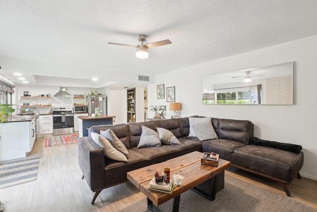 living room featuring light wood-style floors, visible vents, and ceiling fan