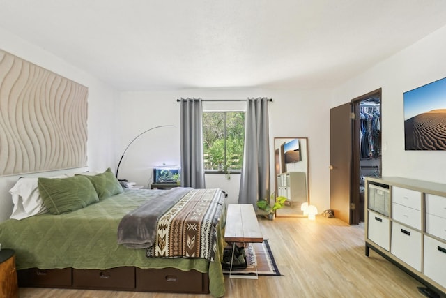 bedroom featuring a walk in closet, a closet, and light wood finished floors