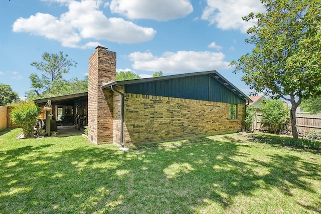 rear view of house with a chimney, a yard, brick siding, and a fenced backyard