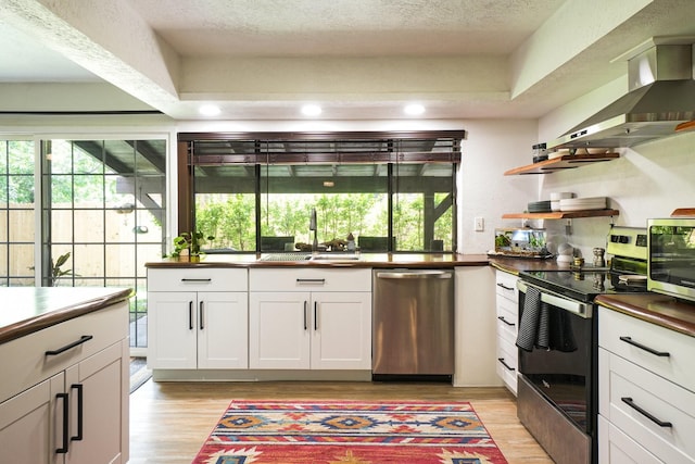 kitchen with a sink, stainless steel appliances, light wood-style flooring, wall chimney range hood, and white cabinetry