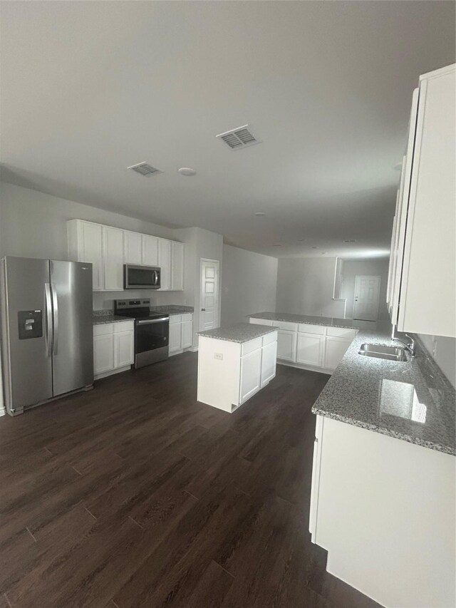 kitchen with light stone counters, stainless steel appliances, visible vents, a sink, and dark wood-style flooring