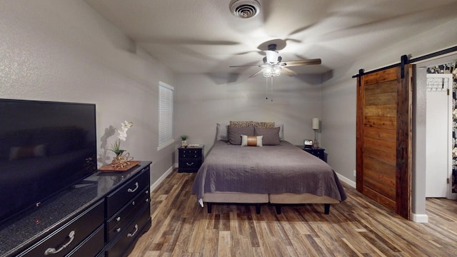 bedroom with a barn door, baseboards, wood finished floors, and visible vents