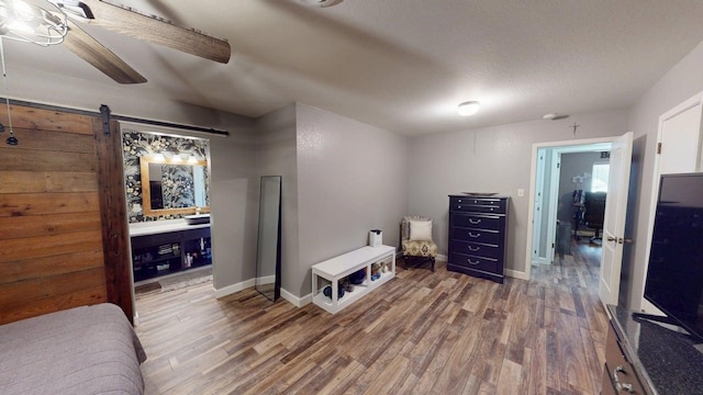 bedroom with a barn door, baseboards, wood finished floors, and ensuite bathroom