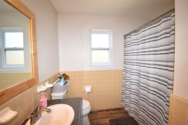 full bathroom with a wainscoted wall, wood finished floors, toilet, a sink, and tile walls