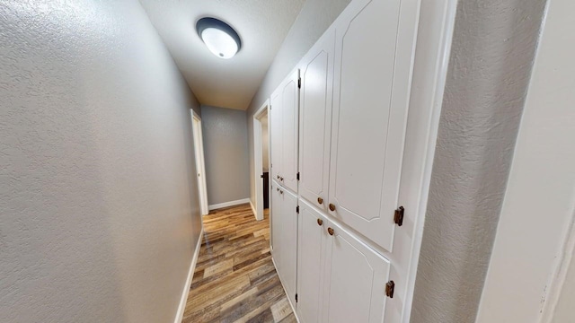 corridor with baseboards, a textured wall, and light wood-style flooring