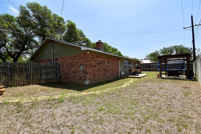 view of property exterior with a pergola, a chimney, a lawn, a fenced backyard, and brick siding
