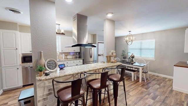 kitchen with island exhaust hood, light wood finished floors, an inviting chandelier, appliances with stainless steel finishes, and white cabinetry