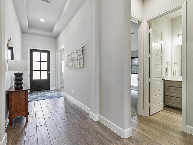 entryway featuring a raised ceiling, wood finished floors, visible vents, and baseboards