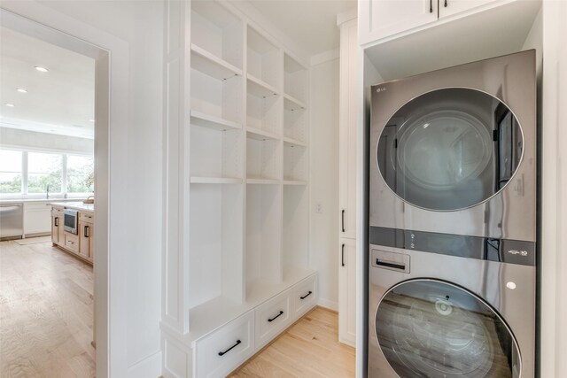 laundry area with light wood finished floors, stacked washer / dryer, recessed lighting, and cabinet space