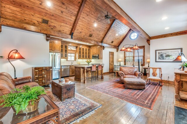living area featuring baseboards, light wood-style flooring, visible vents, and beam ceiling