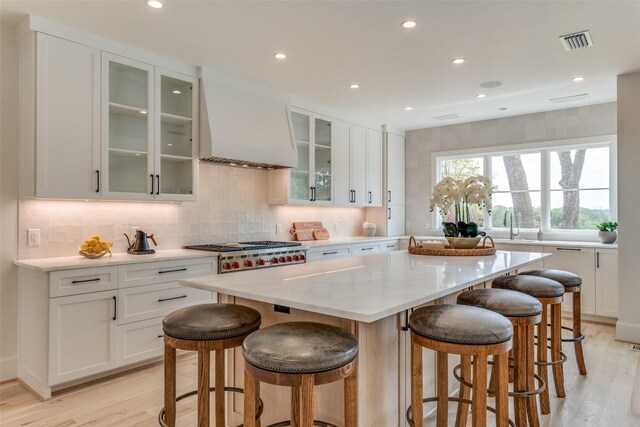 kitchen featuring visible vents, light wood-style floors, custom range hood, and tasteful backsplash