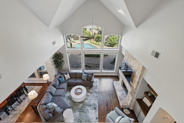 living room featuring visible vents, high vaulted ceiling, wood finished floors, and a stone fireplace