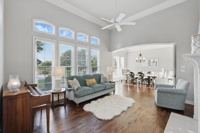living area featuring arched walkways, wood finished floors, ornamental molding, ceiling fan with notable chandelier, and a high ceiling