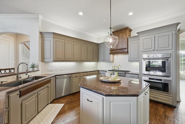 kitchen featuring arched walkways, dark stone counters, stainless steel appliances, a sink, and crown molding