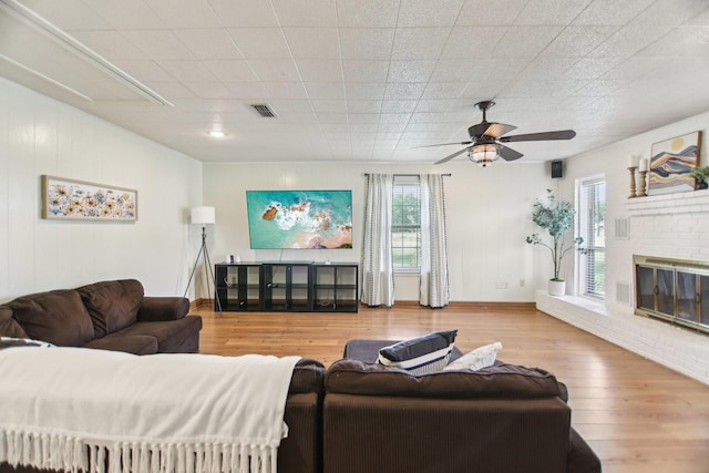 living room with a ceiling fan, wood finished floors, a fireplace, baseboards, and visible vents
