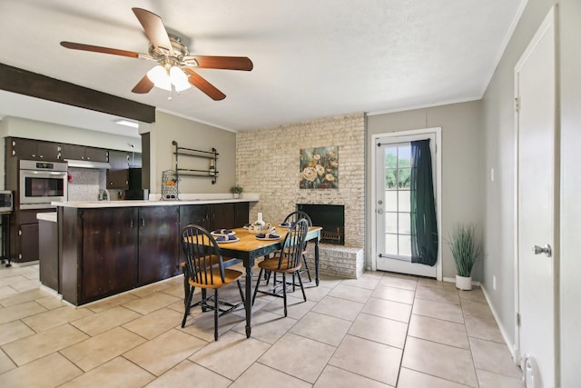 dining area featuring light tile patterned floors, a brick fireplace, ceiling fan, and crown molding