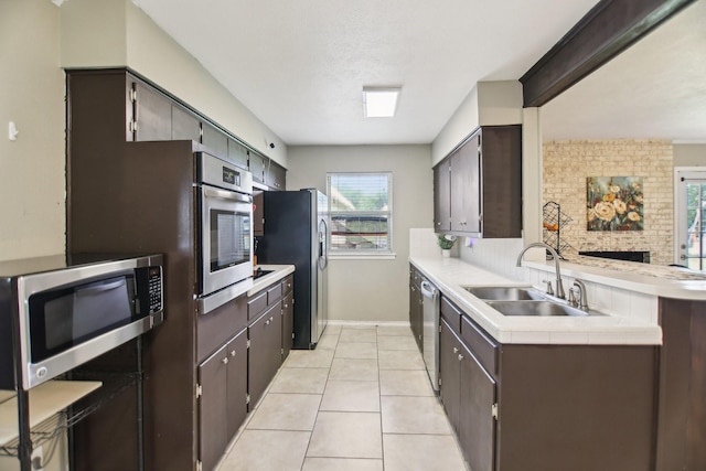 kitchen featuring dark brown cabinets, a sink, light tile patterned flooring, stainless steel appliances, and a peninsula
