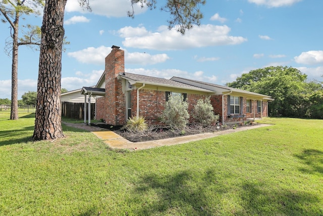 view of side of property featuring brick siding, a yard, a chimney, and fence