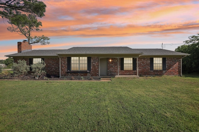 ranch-style house with a chimney, brick siding, a shingled roof, and a front yard