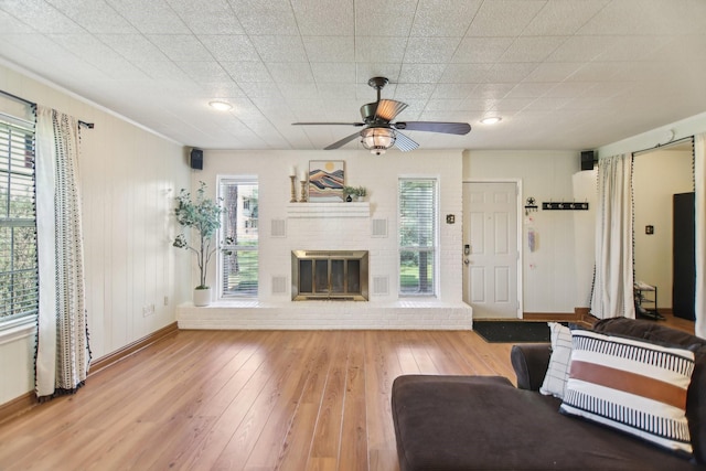 living area with baseboards, a fireplace, ceiling fan, and wood-type flooring