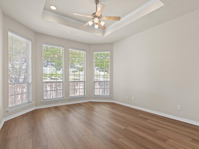 spare room with a tray ceiling, wood finished floors, visible vents, a ceiling fan, and ornamental molding