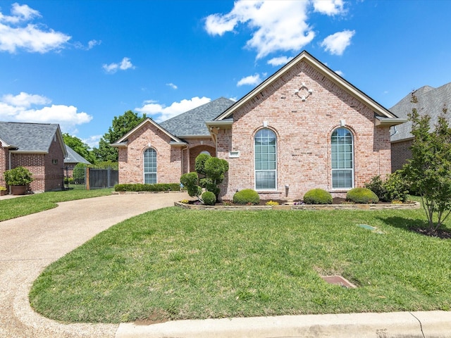 view of front of house featuring concrete driveway, fence, a front yard, brick siding, and roof with shingles