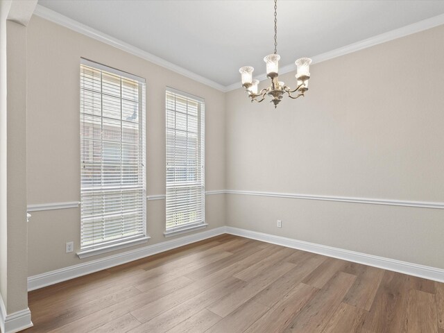 spare room with wood finished floors, a wealth of natural light, a notable chandelier, and crown molding