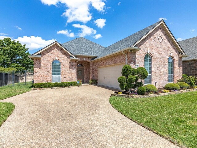 french provincial home with brick siding, roof with shingles, a front yard, and fence