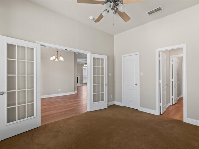carpeted empty room with ceiling fan with notable chandelier, french doors, visible vents, and a high ceiling
