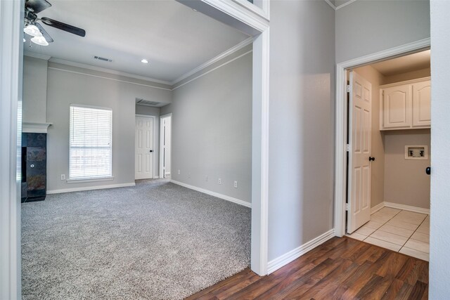 spare room featuring a tiled fireplace, baseboards, visible vents, a ceiling fan, and crown molding