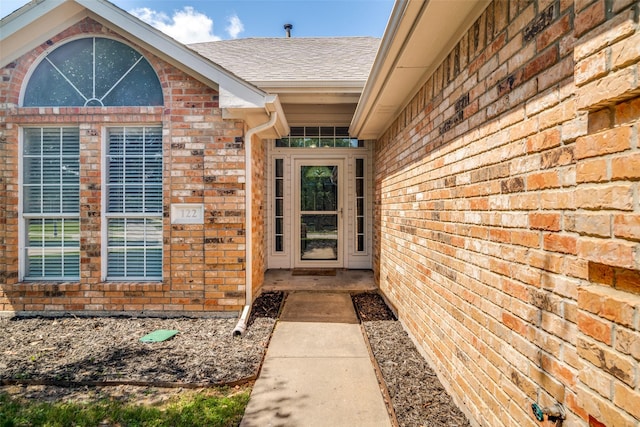 view of exterior entry featuring brick siding and roof with shingles