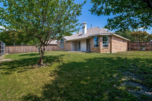 rear view of house with a lawn, a fenced backyard, a chimney, and brick siding