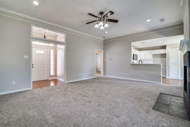 unfurnished living room featuring ornamental molding, baseboards, a ceiling fan, and carpet