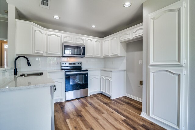 kitchen with wood finished floors, a sink, decorative backsplash, appliances with stainless steel finishes, and visible vents