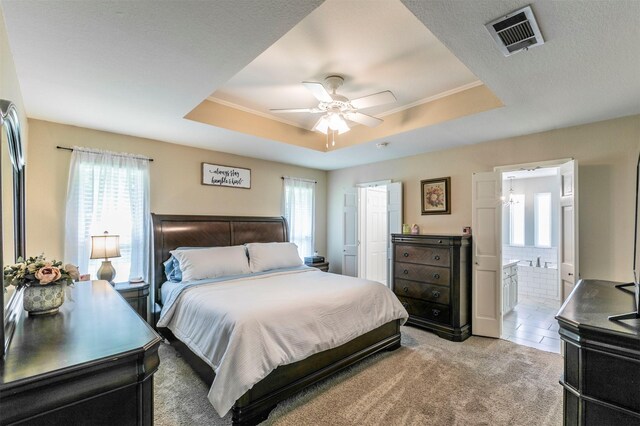 bedroom with a raised ceiling, visible vents, connected bathroom, light colored carpet, and ceiling fan