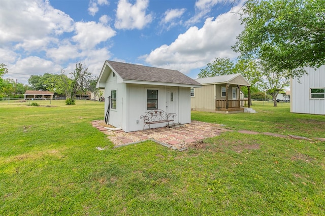 back of property with an outdoor structure, a yard, and a shingled roof