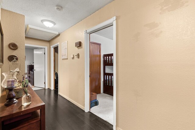 corridor with dark wood finished floors, a textured wall, a textured ceiling, and baseboards
