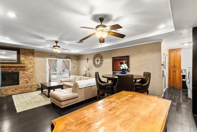 living room featuring dark wood finished floors, a brick fireplace, a tray ceiling, and ceiling fan