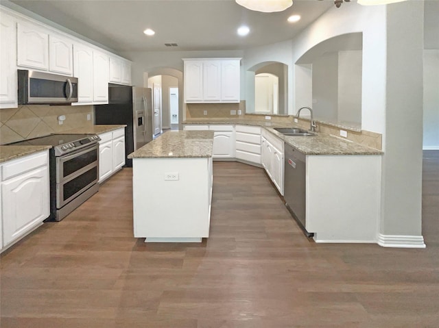 1005 Lake Hollow Dr, Little Elm, TX 75068 - kitchen with arched walkways, stainless steel appliances, white cabinets, a sink, and a center island