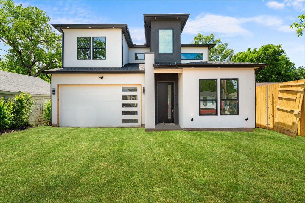 back of house with driveway, fence, an attached garage, a lawn, and stucco siding