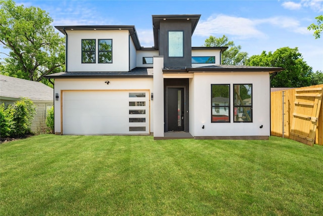 back of house with driveway, fence, an attached garage, a lawn, and stucco siding