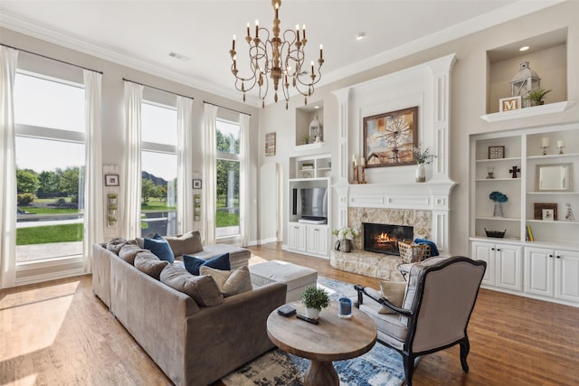 living room featuring an inviting chandelier, a stone fireplace, visible vents, light wood-style floors, and built in shelves