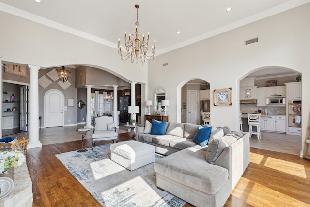 living room with light wood-style floors, visible vents, crown molding, and an inviting chandelier