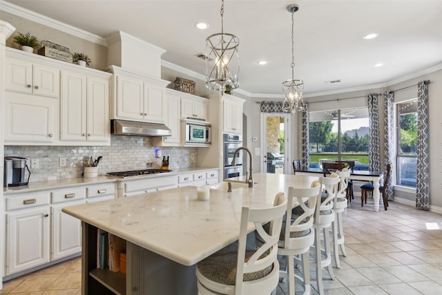 kitchen with decorative backsplash, light tile patterned floors, a center island with sink, under cabinet range hood, and visible vents