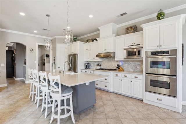kitchen featuring decorative backsplash, light tile patterned flooring, arched walkways, appliances with stainless steel finishes, and under cabinet range hood